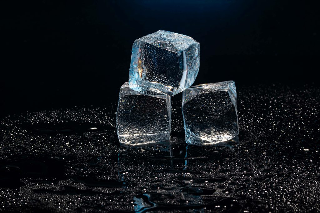 Three clear ice cubes stacked in a dark setting with water droplets for a cooling effect.